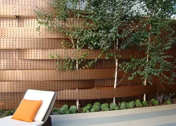 Perforated Metal Fence: Perforated metal sheets woven like basketwork, with trees growing through the gaps left in the run