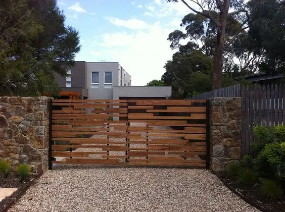 Mid-Century Modern front gate: Steel and timber up front, stacked-stone posts and a gravel drive behind