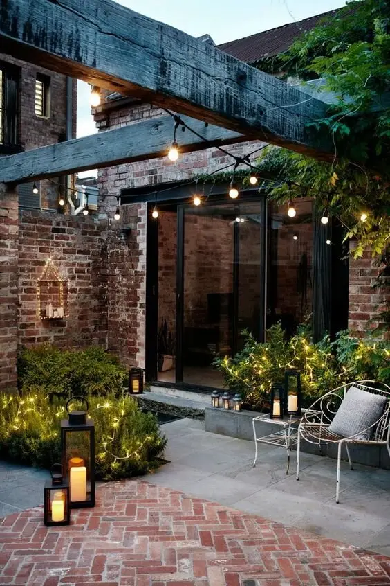 Rustic Bricks deck and patio: Brick paving, exposed timber beams, string lights overhead. Storm lanterns and vintage iron