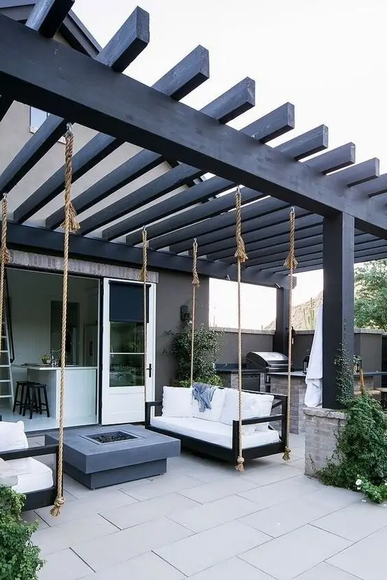 Swing Seats deck and patio: Sofa swings hung from a black steel pergola, arranged around a concrete fire pit. Confirm the