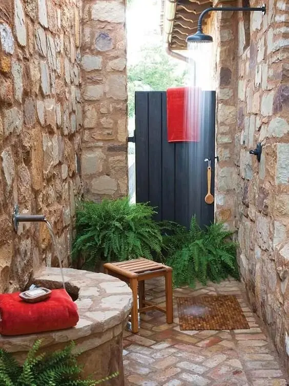 Warm Mallorca outdoor shower: Craggy stone, brick floors, a free-flowing spout and a circular well, with ferns softening the
