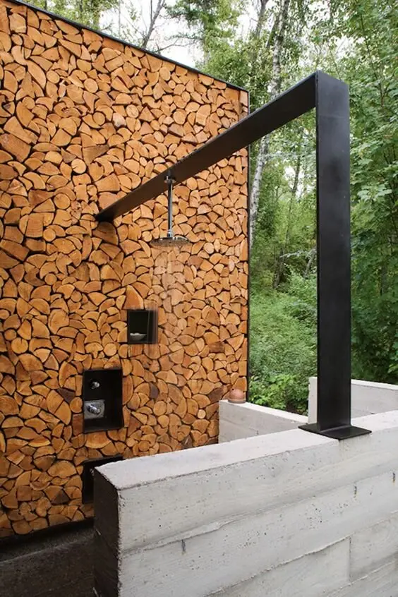Wood Pile Wall outdoor shower: A wall built like a neat firewood stack, with a black steel beam holding the head and shelves