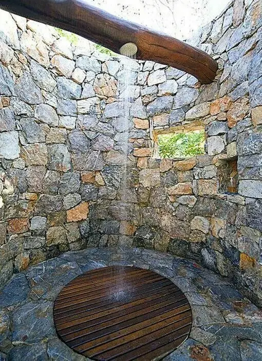 Beam and Stones outdoor shower: A stacked stone circle, flagstones, a round timber mat and a rain head hung off a raw beam
