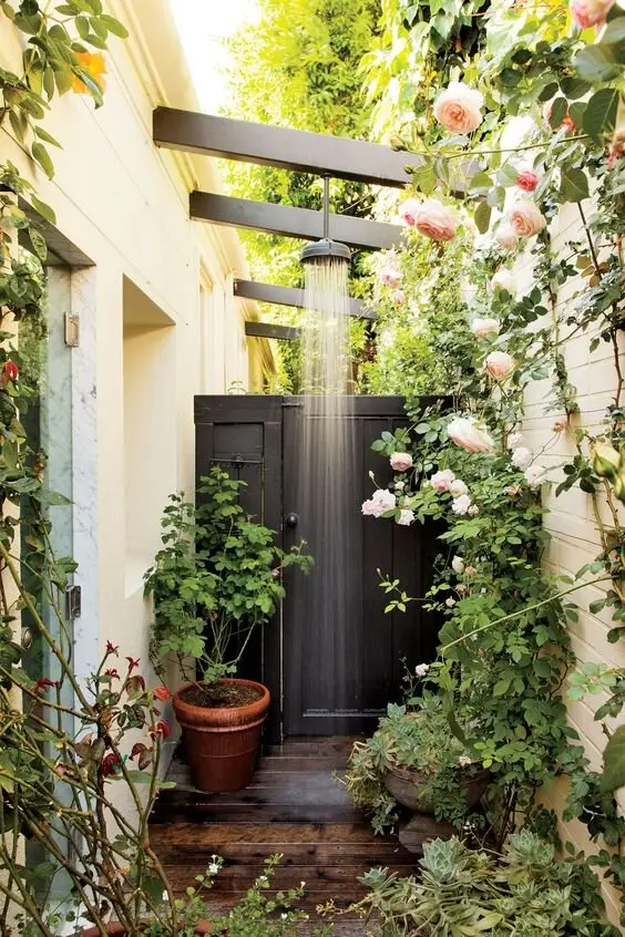 A Rosy Retreat outdoor shower: A corner nook with rafters and timber floors, ringed with potted roses. The shower waters