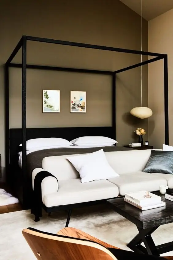 The Private Gentleman bedroom: Four-poster bed, tan walls, white rugs and a small seating corner