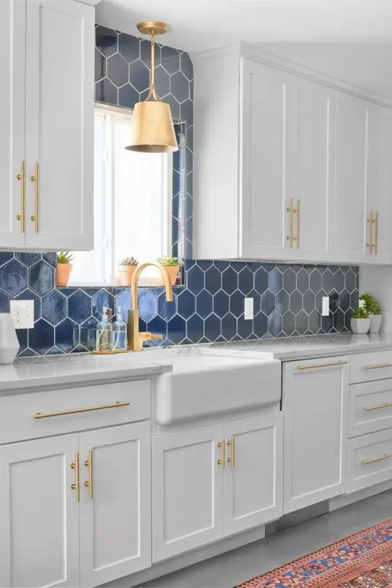 Elegant Farmhouse farmhouse kitchen: White interiors with gold hardware and a blue beehive-pattern tiled wall. The hex tiles