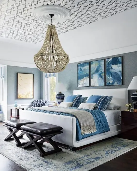 Hamptons Glam coastal bedroom: A huge shell chandelier, a wave-patterned ceiling, stone-grey walls and coordinated blue