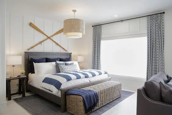 Seaside Sanctuary coastal bedroom: A big bed, a reed storage box doing bench duty, and a pair of paddles on the wall. One