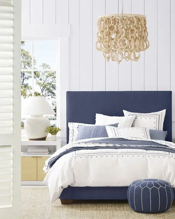 Elegant Mediterranean coastal bedroom: Vertical shiplap, jute rugs, white shutters and a blue and white bed under a serious