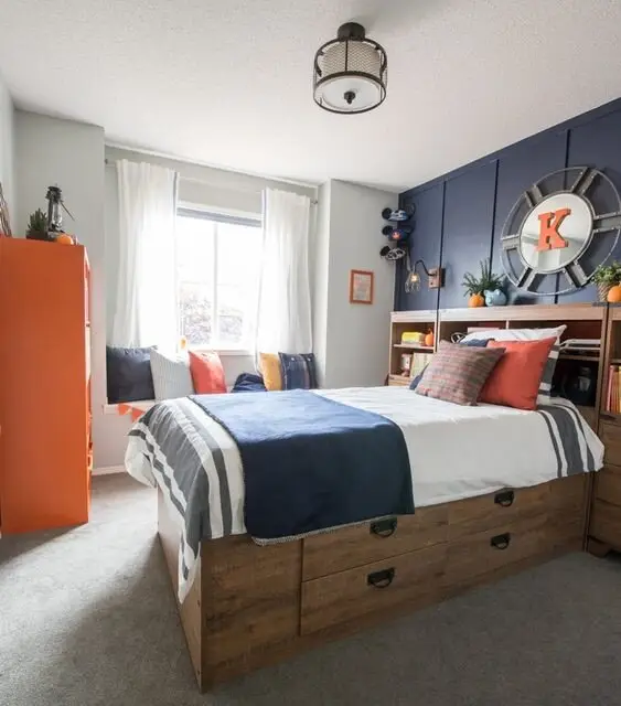 Young Sailor coastal bedroom: A timber box bed with drawers underneath, a navy accent wall and a window seat piled with