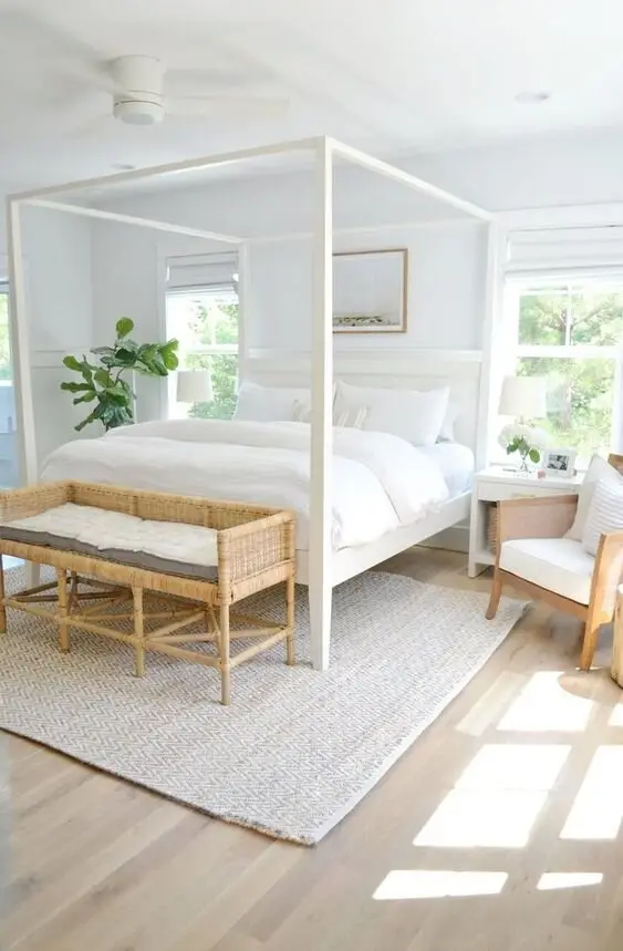 White Four-Poster coastal bedroom: A white four-poster, rattan furniture and bare boards under big open windows. Farmhouse