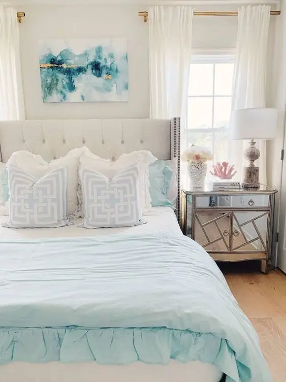 Coastal Elegance coastal bedroom: A mirrored night table, tufted headboard and vintage lamp on the formal side; white