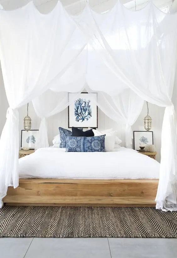 Canopied Boho coastal bedroom: A four-poster dressed in wispy white curtains, with blue accents, silver Moroccan lamps and